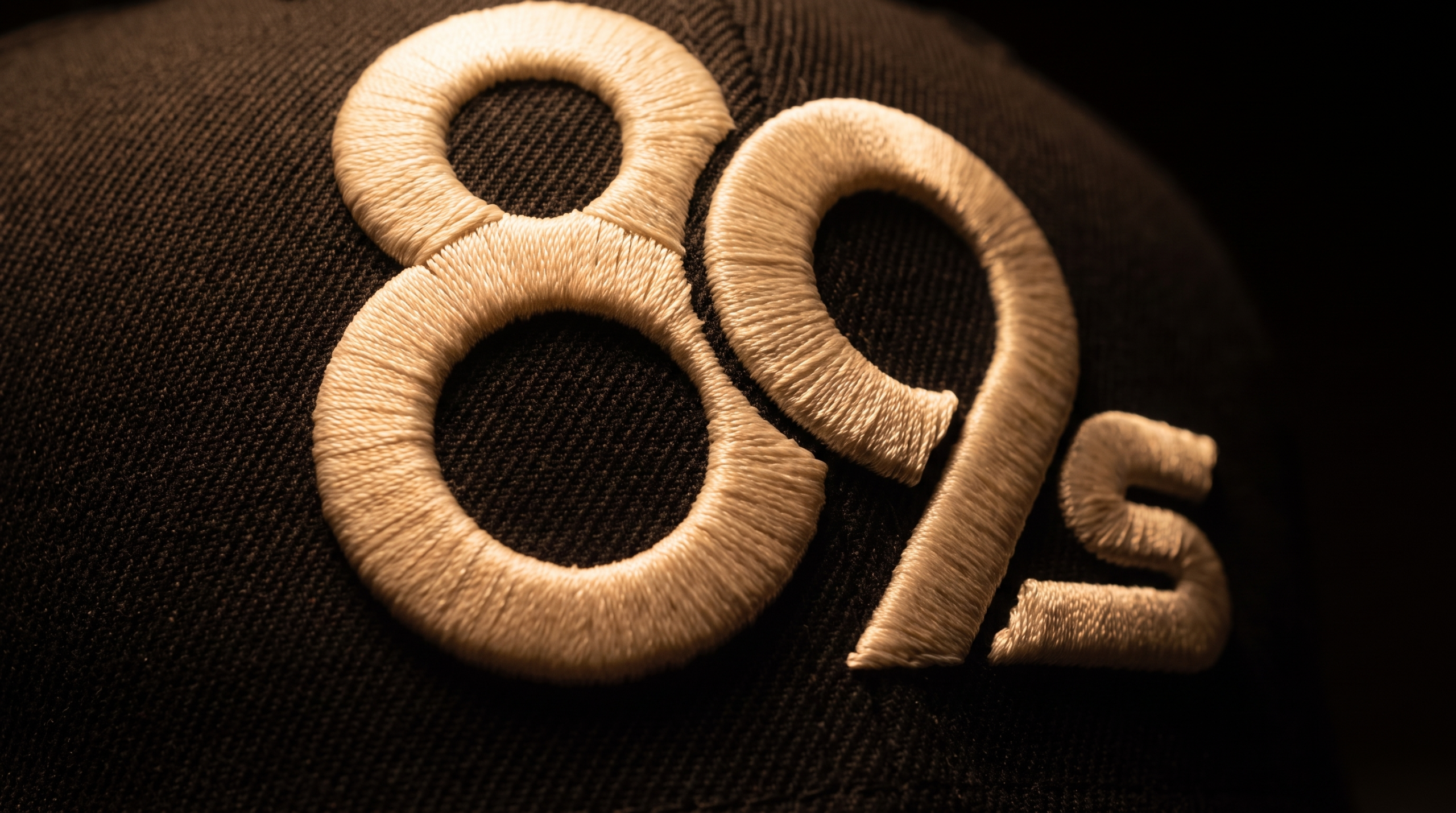 Close-up of the 89s monogram embroidered in cream thread on a black poker cap