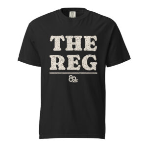 The Reg tee in black, THE REG printed in worn cream block letters across the chest.
